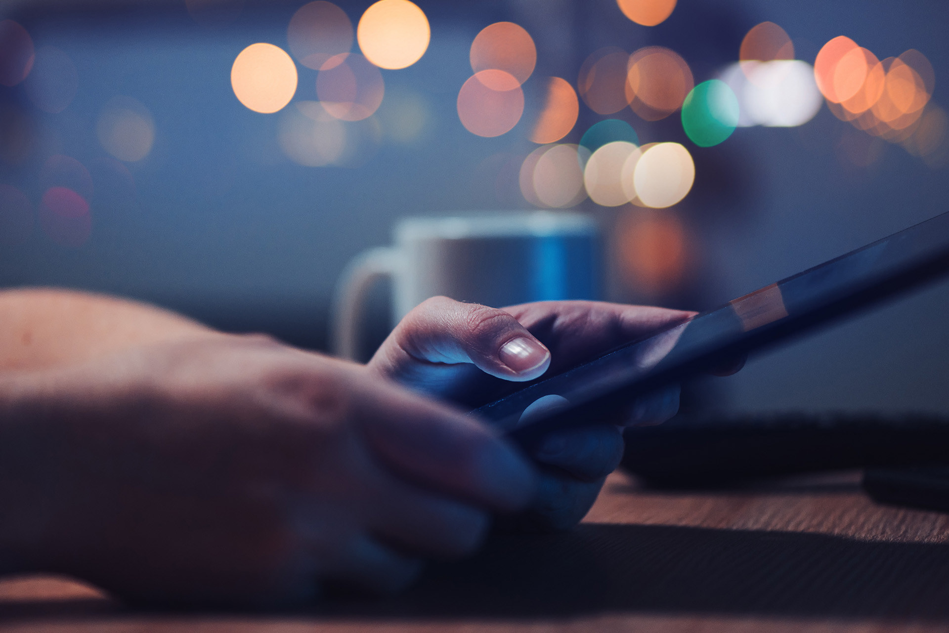 In a dimly lit setting, hands hold a smartphone or tablet, likely browsing web design tips, with colorful bokeh lights blurred in the background and a cup on the table.