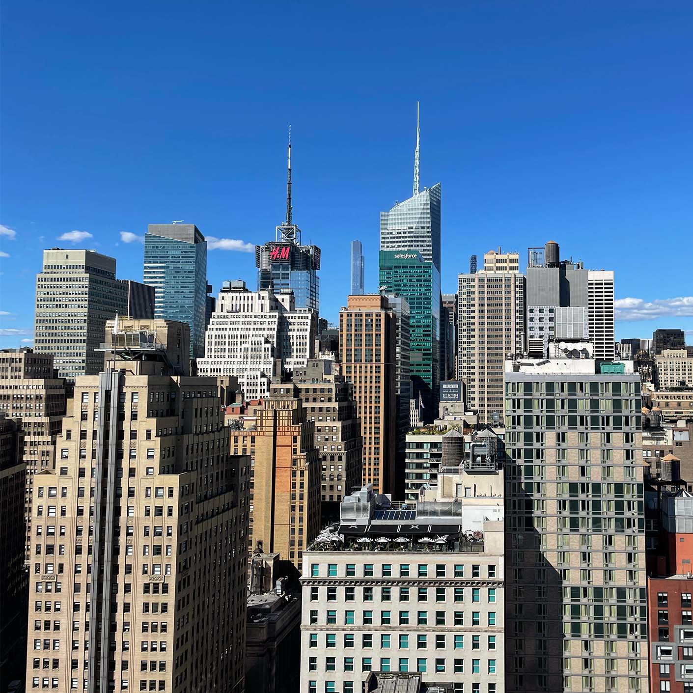 A cityscape of New York City under a clear blue sky, featuring a mix of modern and classic skyscrapers. Prominent buildings, including a tower with the number "4" on it, create a dynamic urban skyline.