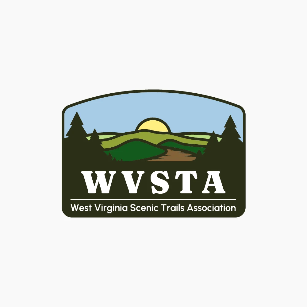 Logo for the West Virginia Scenic Trails Association (WVSTA) featuring stylized green hills, a sun on the horizon, and silhouettes of pine trees. The text "WVSTA" is prominently displayed, with "West Virginia Scenic Trails Association" below.